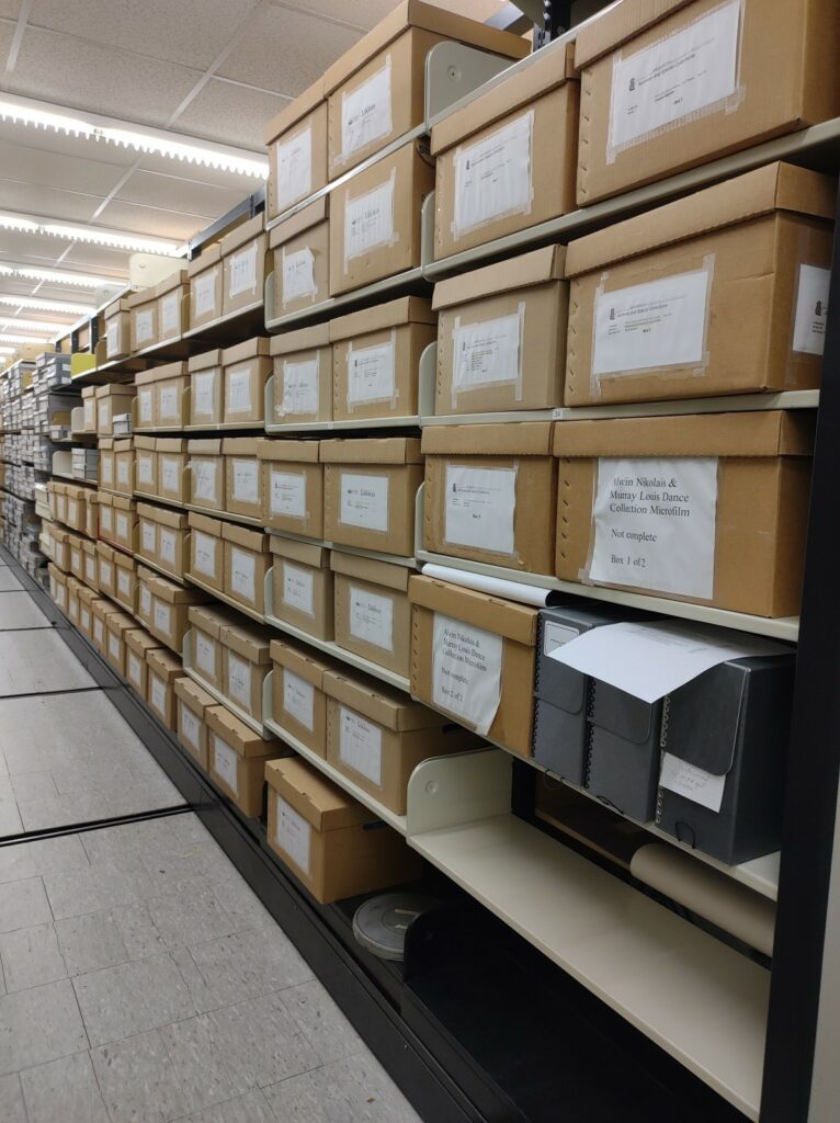 Brown boxes line a long long  library shelf, each with a label about the Nikolais /Lewis collection of OU Libraries. 