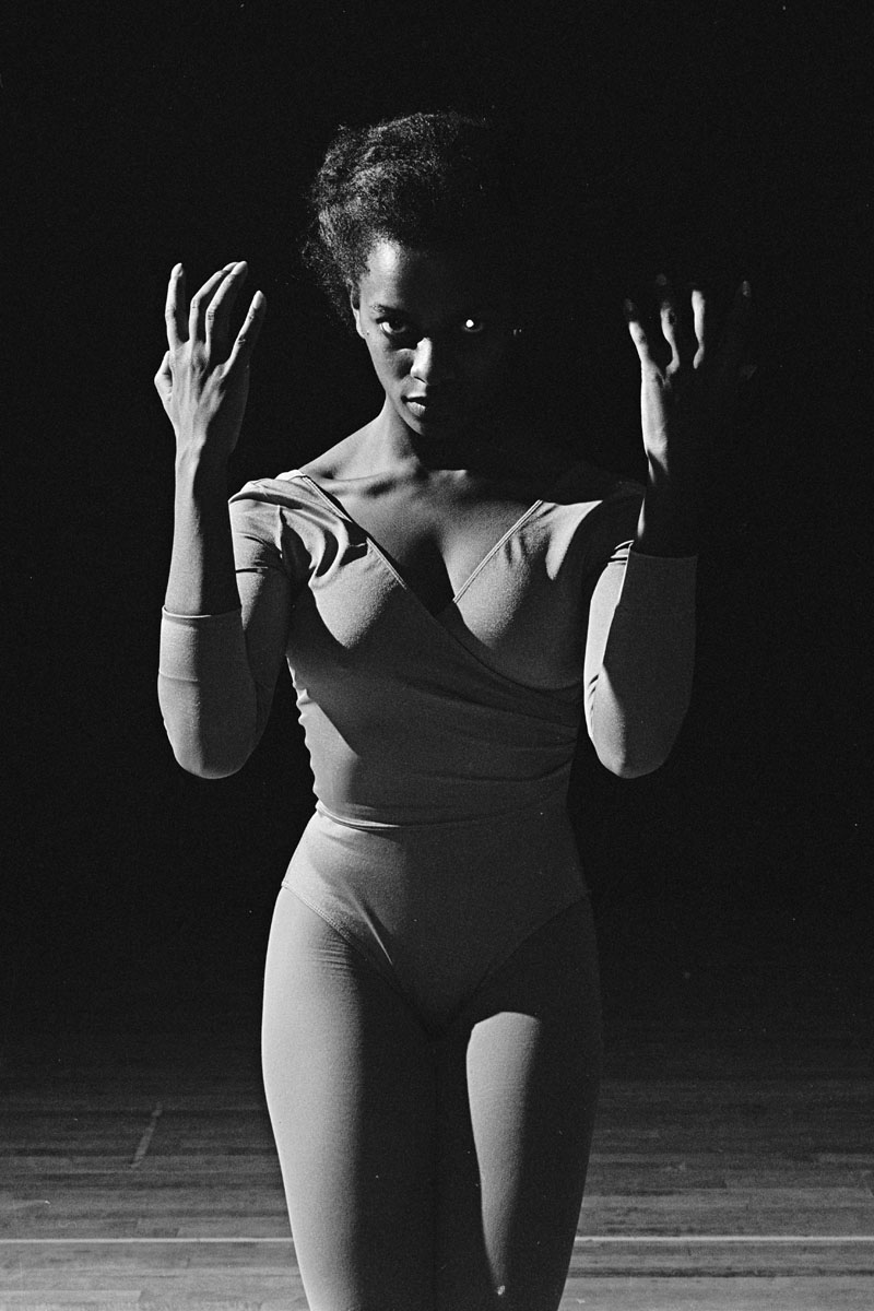 Dancer posing in a leotard and staring into the camera with dramatic stage lighting