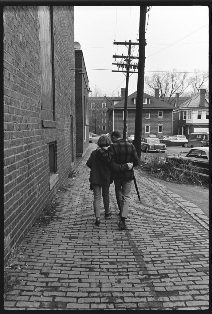 Two people photographed from behind, embracing while walking in an alley, 1967
