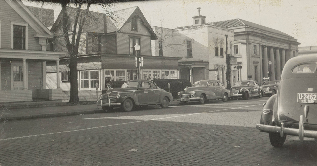 Black and white photo of street with buildings and cars parked, circa 1940