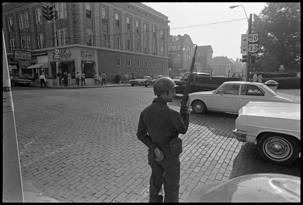View of street and cars at intersection with National Guard member holding a rifle