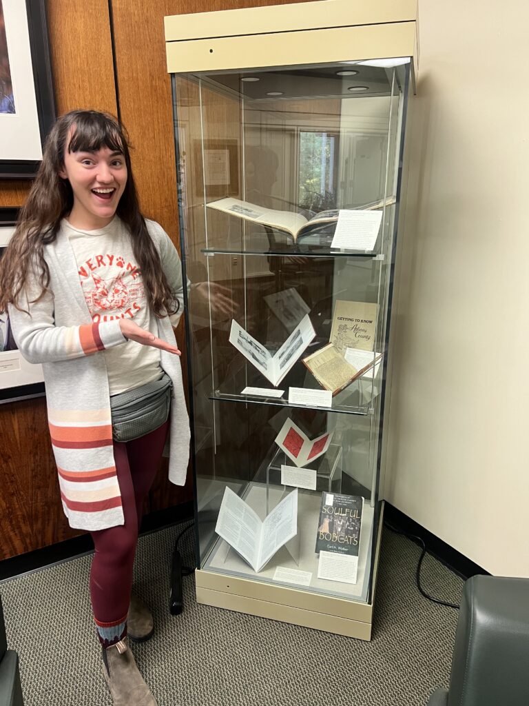 Alexis stands next to a glass display case of her rare books exhibit exploring the history of Athens. 