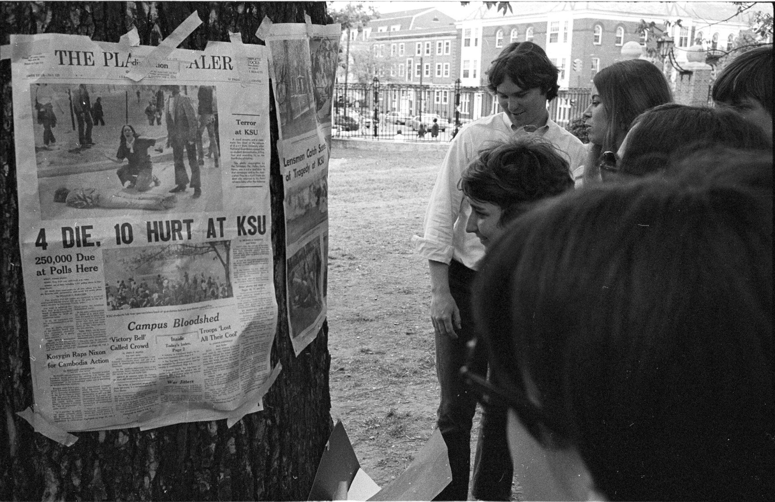 Students reading newspaper posted on a tree with headline about Kent State shootings