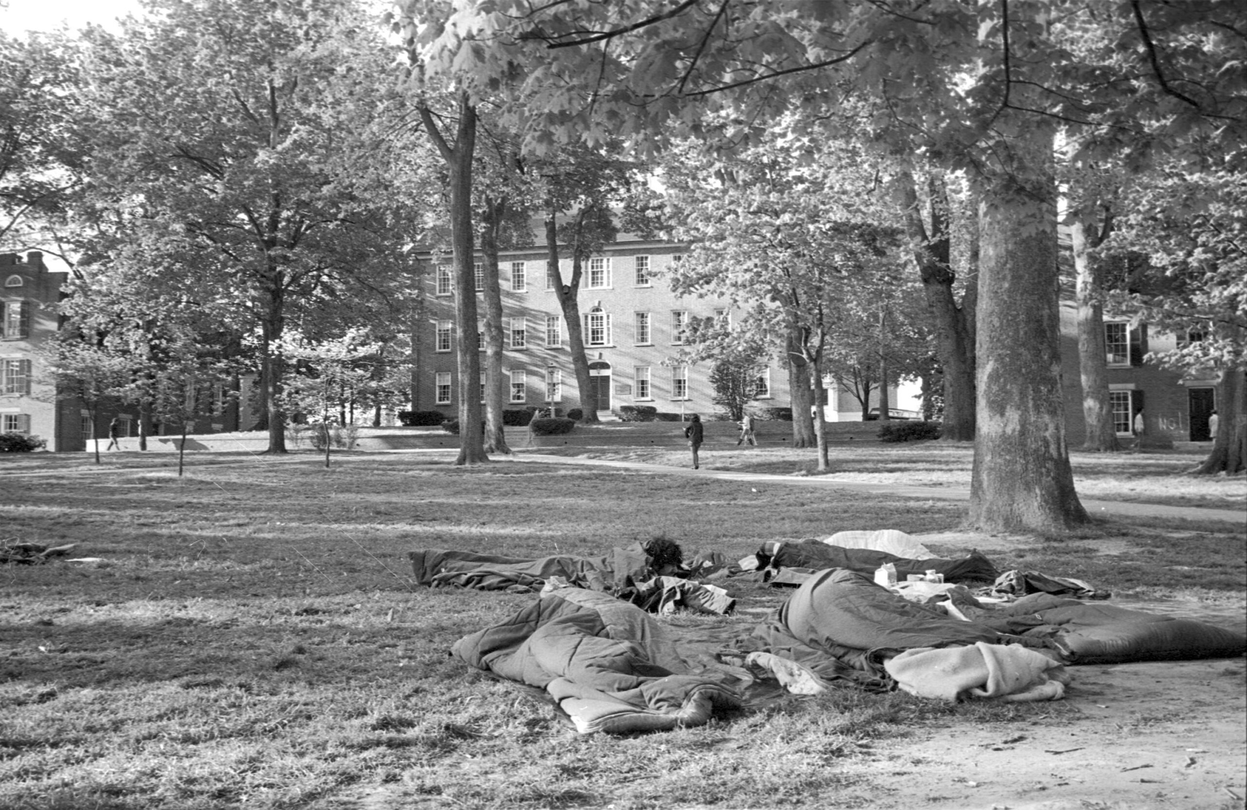Several people sleeping with blankets on the College Green