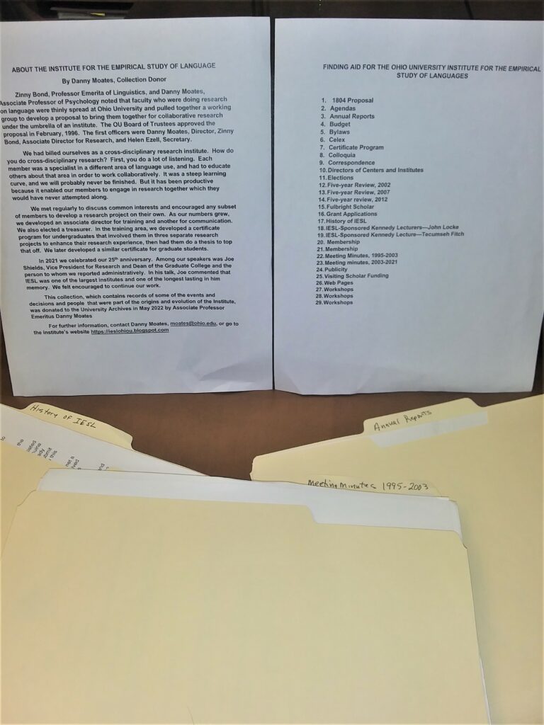 two pieces of paper with information about the collection are placed vertically above three folders fanned out below them