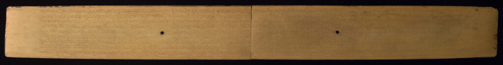 Front side of palm leaf manuscript with very faint, inscribed text that is more visible where light is illuminating the left side