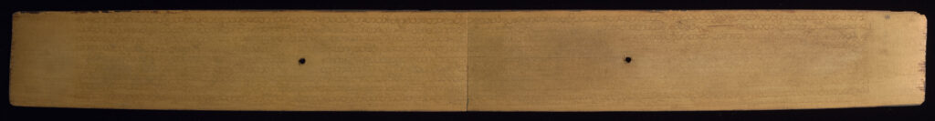 Front side of palm leaf manuscript with very faint, inscribed text that is more visible where light is illuminating the right side