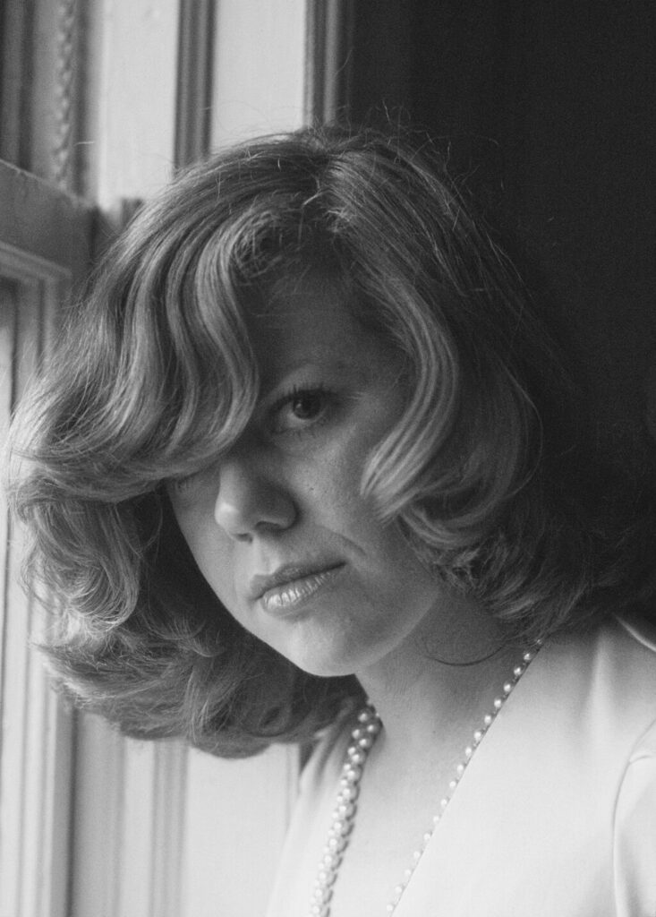 Black and white head-and-shoulders portrait of Erica Jong beside a window with hair swept across one eye