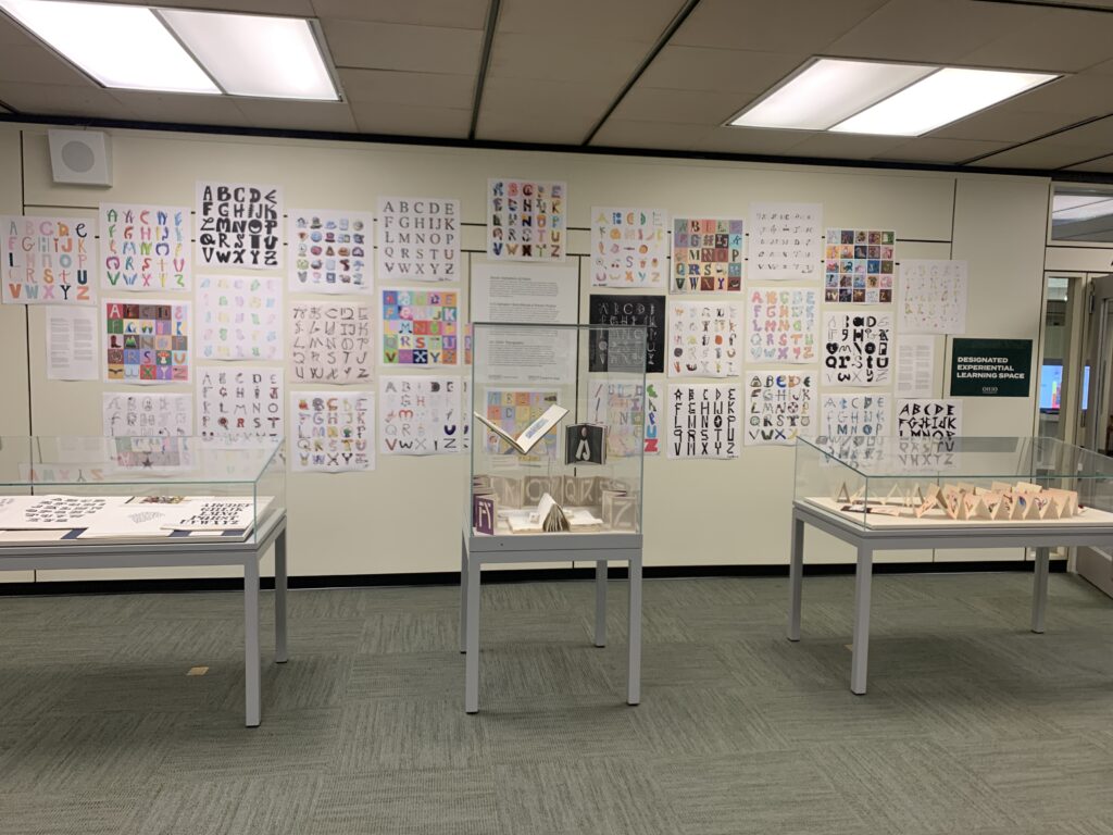 View of the alphabet posters on the wall, and display cases containing example typographical texts and artists' books from the rare book collection