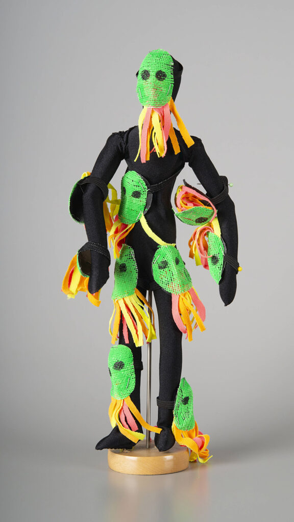 9-inch tall wooden mannequin wearing dance costume consisting of a black bodysuit with numerous tassled, neon face masks attached