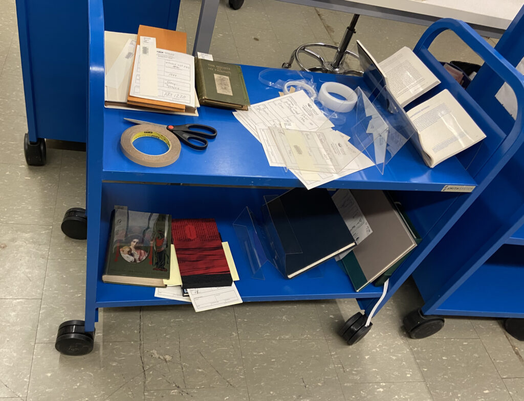 A cart from rare books holding the materials for my exhibit prior to placing them on display, along with some of the tools we use for display purposes. 