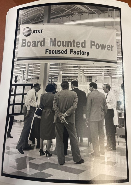 Dory standing among a group of men under a banner that reads AT&T Board Mounted Power Focused Factory.