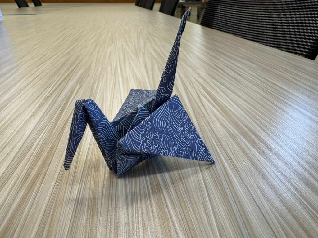 Origami crane made of blue paper covered in white swirly lines.