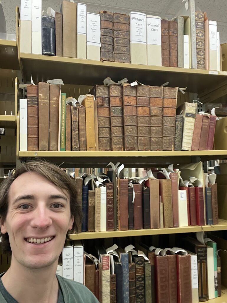 Shelfie of Zach Bisselberg in front of shelves of leather bound books.