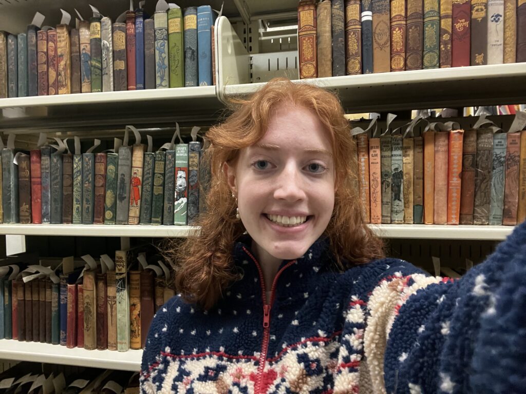 Shelfie of Avery Kumes in front of shelves of colorfully bound books.