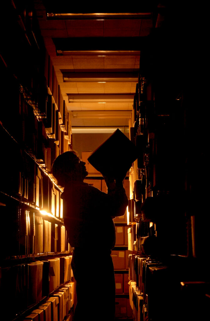 Backlit photo showing outline of Ohio University archivist, Bill Kimok, reaching to place a box on a shelf.