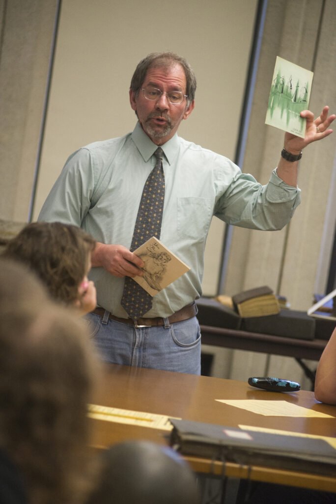 Ohio University archivist, Bill Kimok, addresses high school students during a class visit while holding historical college handbooks up for display.