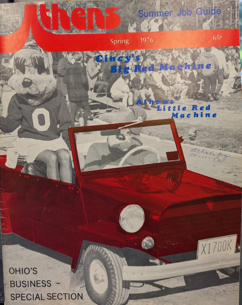 The cover of a magazine with a black and white image of two people dressed in bobcat mascot costumes driving a colorized red King Midget car.