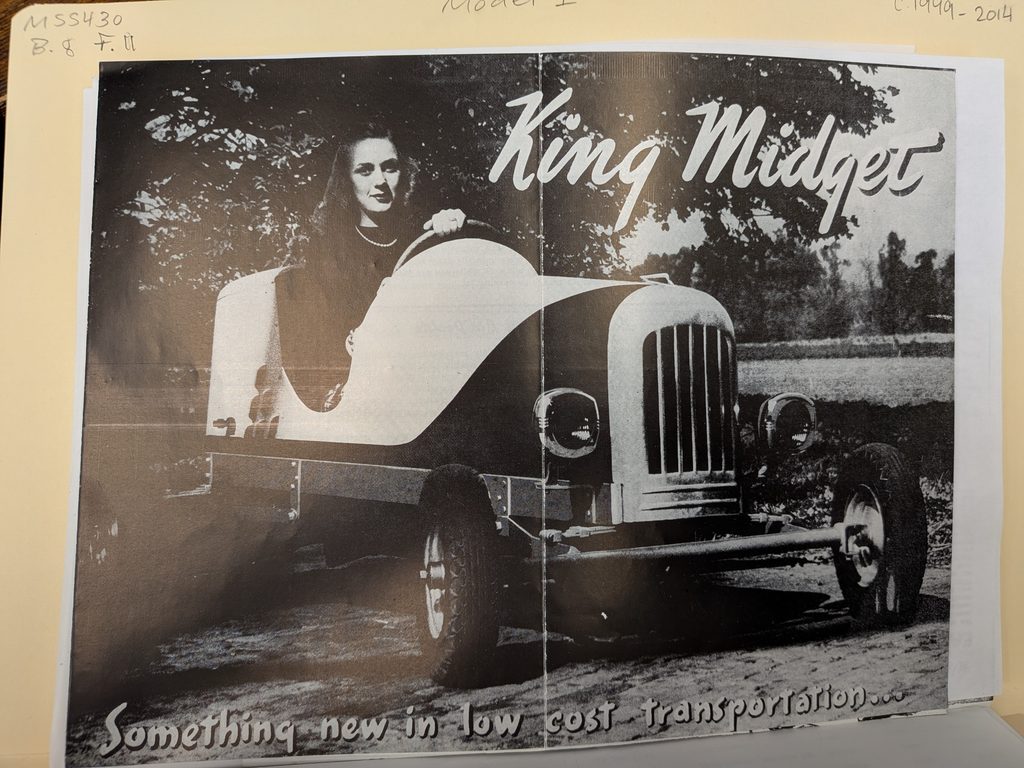 A black and white two page image of a woman in a King Midget model 1 car with the words "Something new in low cost transportation..." at the bottom.