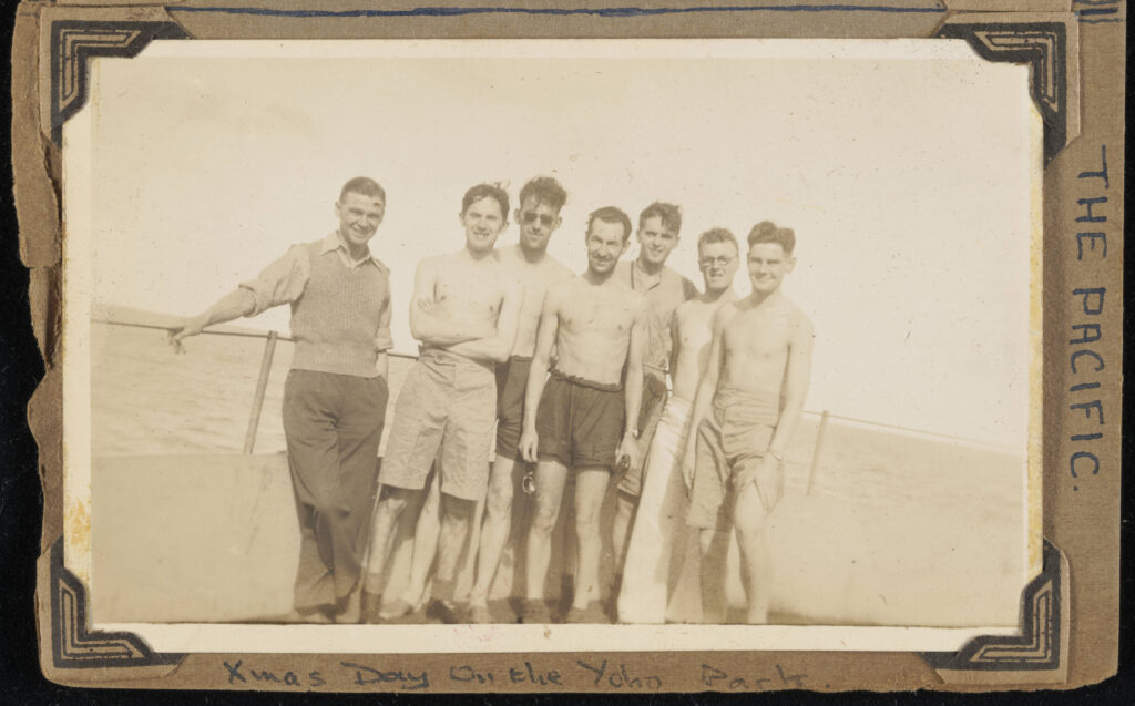 Faded black-and-white album photo of seven men, some without shirts, on a boat at sea and captions that read “The Pacific” and “xmas day on the Yoho Park.”