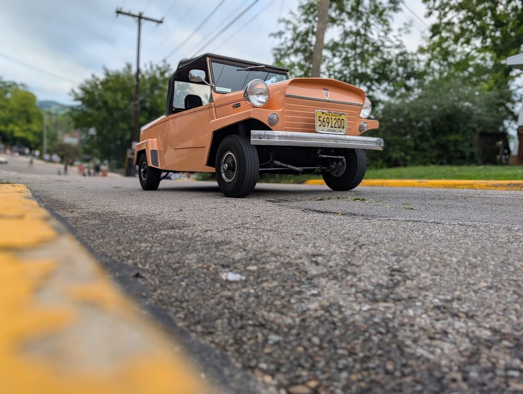 A peach colored King Midget car on the road seen from a below street level angle.