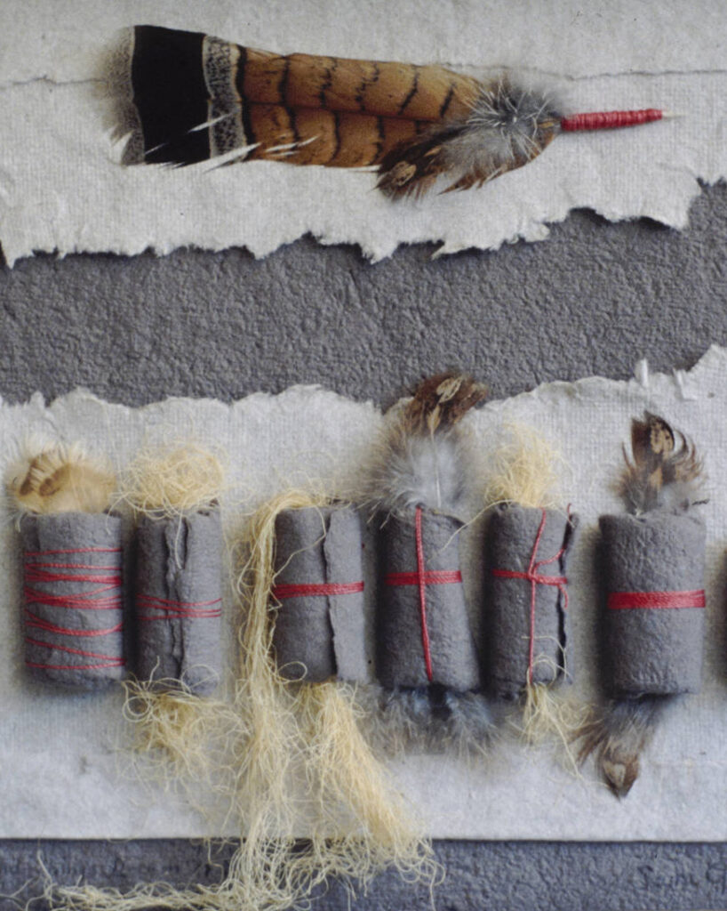 Art work incorporating handmade gray and white paper, red silk thread, natural fibers, and feathers.