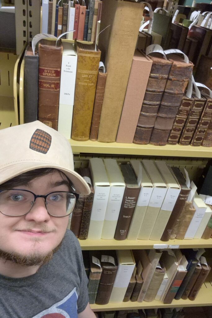 Shelfie of Thomas Raulerson in front of books written by several classical authors, including Ovid, Pliny, Seneca, and Quintilian.