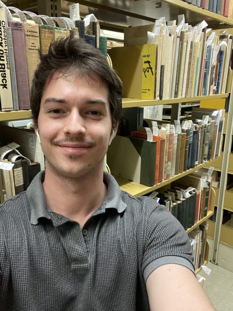 Intern Conrad Burt standing in front of a shelf in the rare books collection.