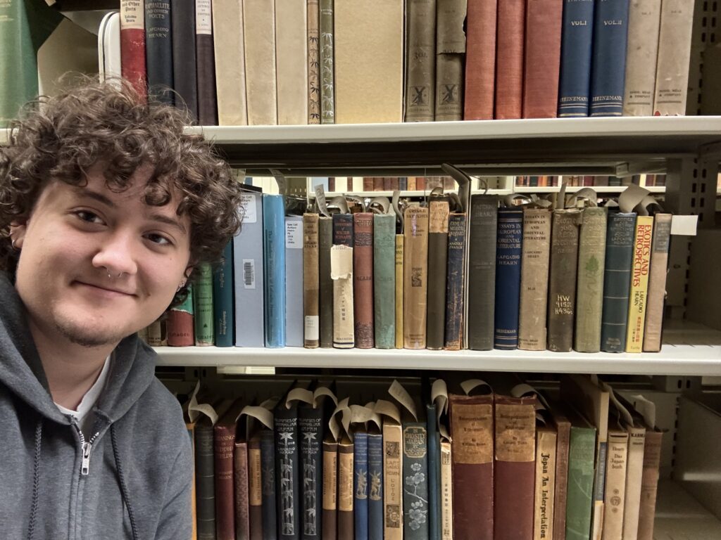 Lucas Honkomp in front of a shelf containing various books included in the Lafcadio Hearn Author’s Collection.