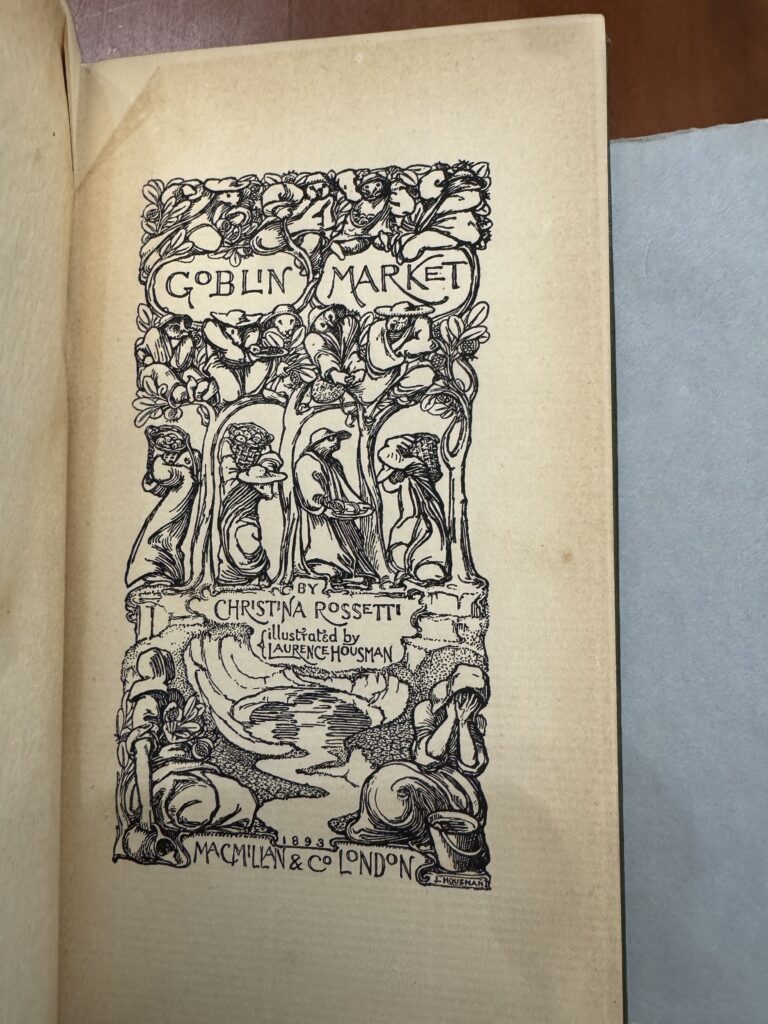A book lies open to the title page which includes an elaborate illustration of woodland creatures in clothing. Text on the page reads: “Goblin Market. By Christina Rosetti. Illustrated by Laurence Housman. 1893. Macmillan & Co. London. 