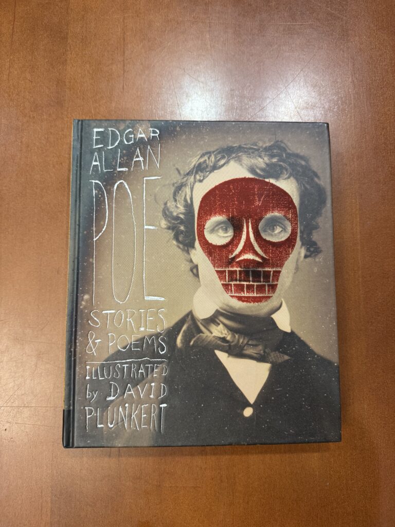 A book lies on a brown table with a large portrait of a man with brown hair; a red skull is overlaid over the face of the man. Text on the left side reads: “Edgar Allan Poe Stories & Poems. Illustrated by David Plunkert.” 